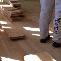 Plankegulv. Tømrersvend i gang med at ligge et gedigent gulv af kraftige fyrretræsplanker i dimensionen 35 x 250mm.