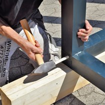 Tømrersvend svinger hammeren og slår en trænagle i ved samling af en traditionel tømmersamling.