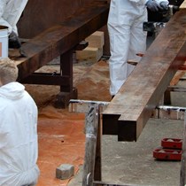 Tømrere i gang med tjæring af tømmer med trætjære. Det dufter af tømrerarbejde.