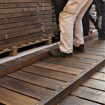 ​Tjærede egeplanker til en træbro. En tømrersvend og en tømrerlærling i gang med samling af et brodæk til en egetræsbro.